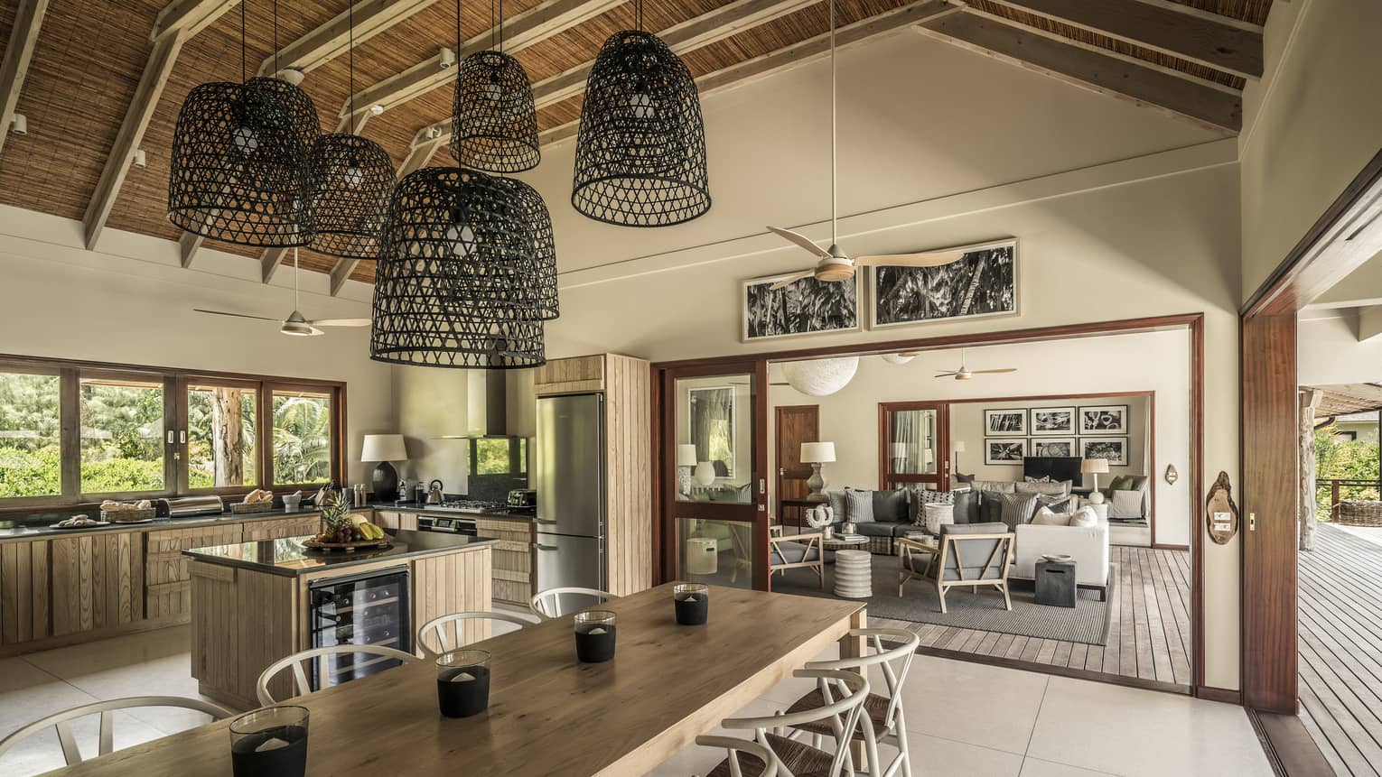 Large basket-like chandeliers hang from gambrel roof over long wood dining table, large kitchen