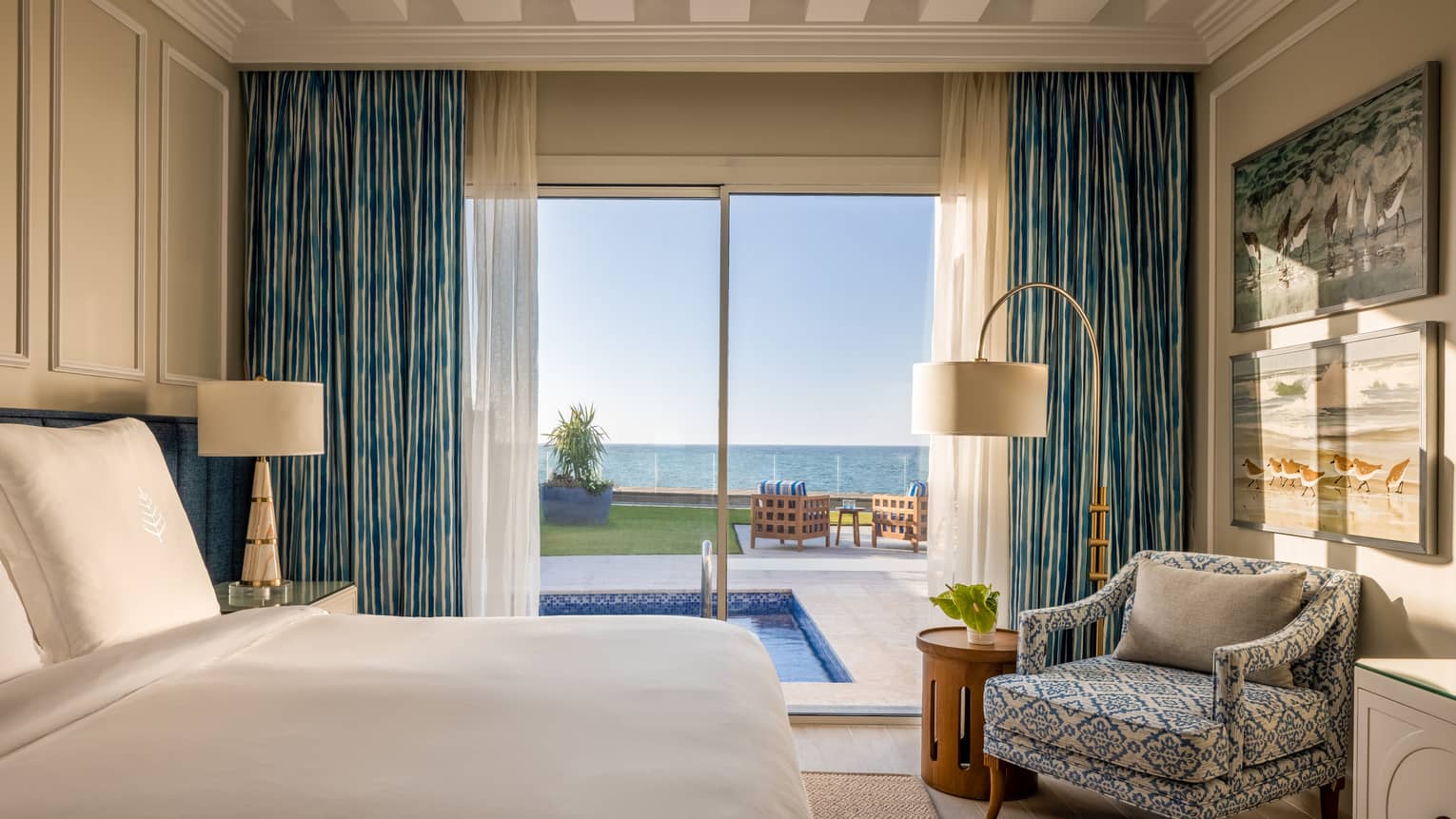 One-Bedroom Beach Villa bedroom with king bed, patterned armchair, sliding glass door to pool