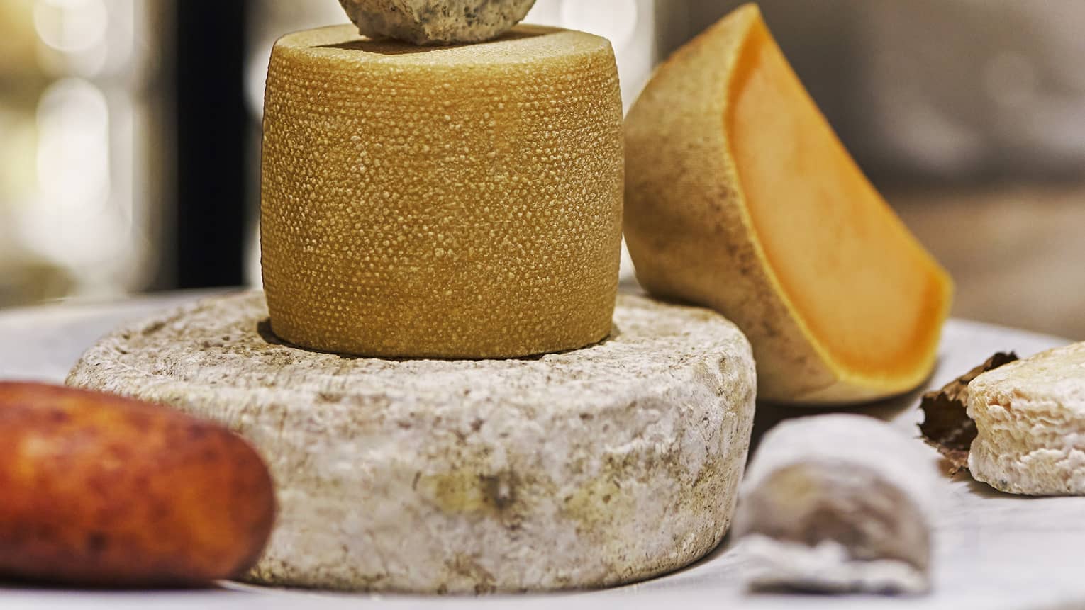 Three wheels of different cheeses stacked on top of each other along with four othe blocks of cheese alongside