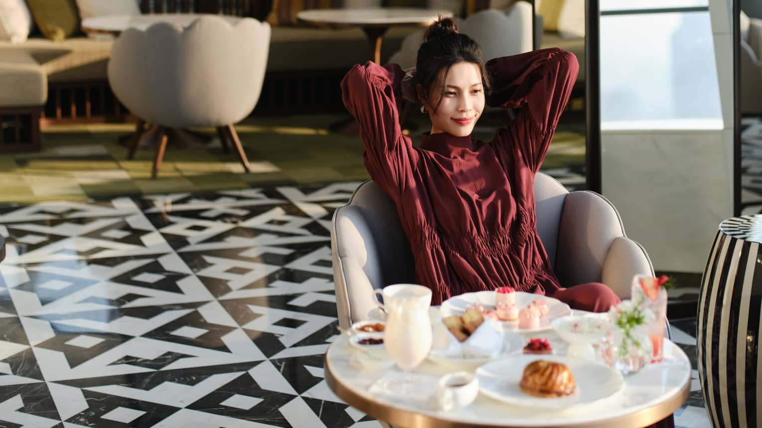 A guest smiles at a table set for tea with dainty pastries and sweets upon a striking black-and-white geometric tiled floor.