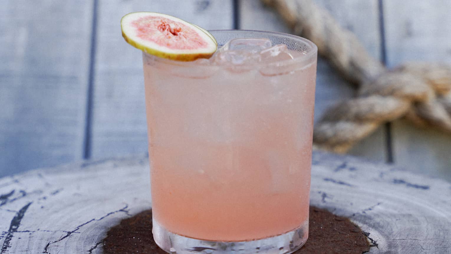 A clear glass holds a pale pinkish drink with a garnish on top.