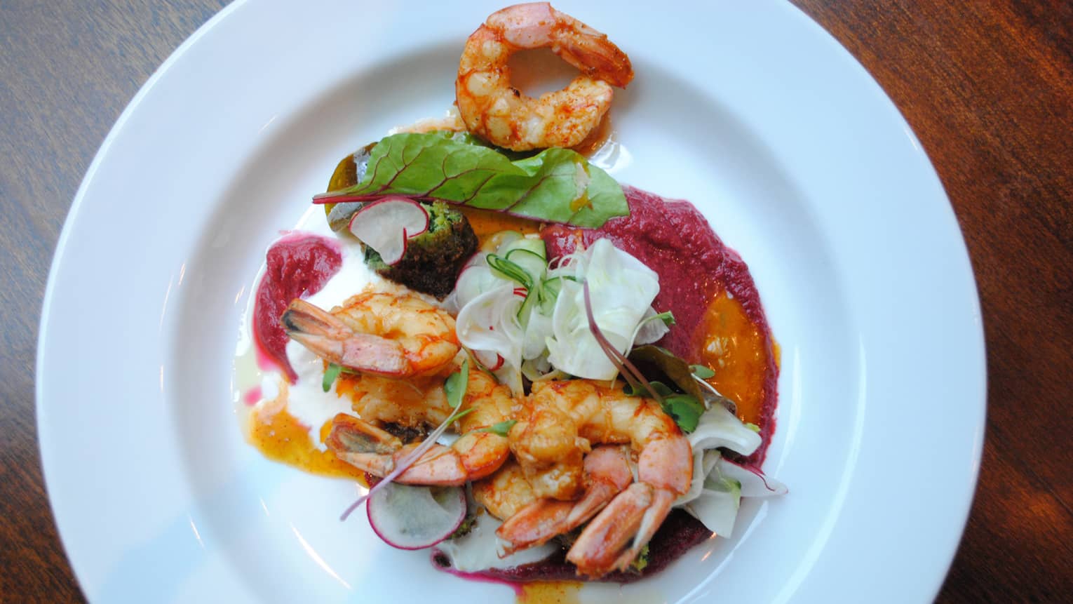 A shrimp dish is served with radishes, greens and a creamy sauce