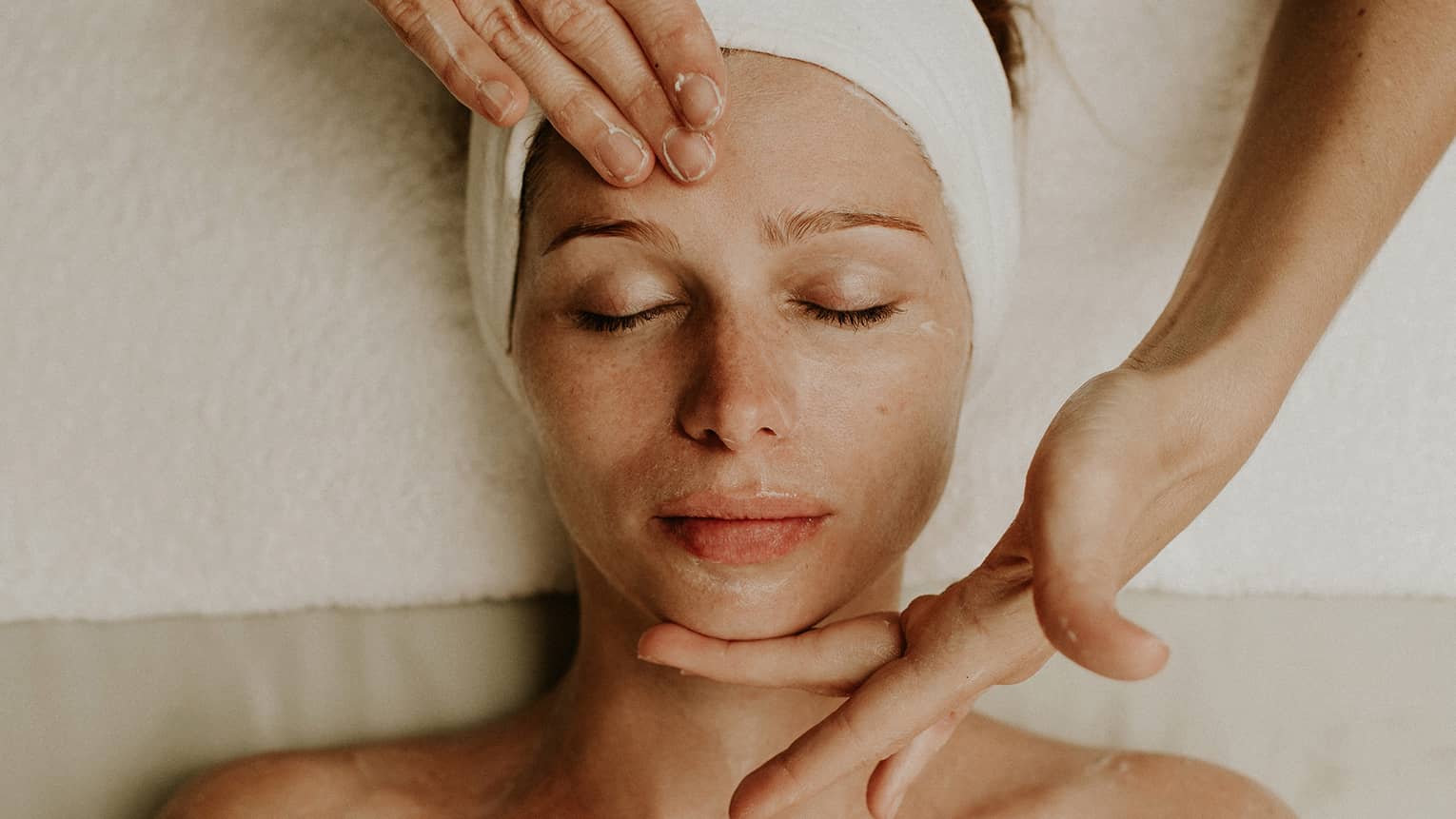 Person receiving a relaxing facial massage with eyes closed and head wrapped in a towel