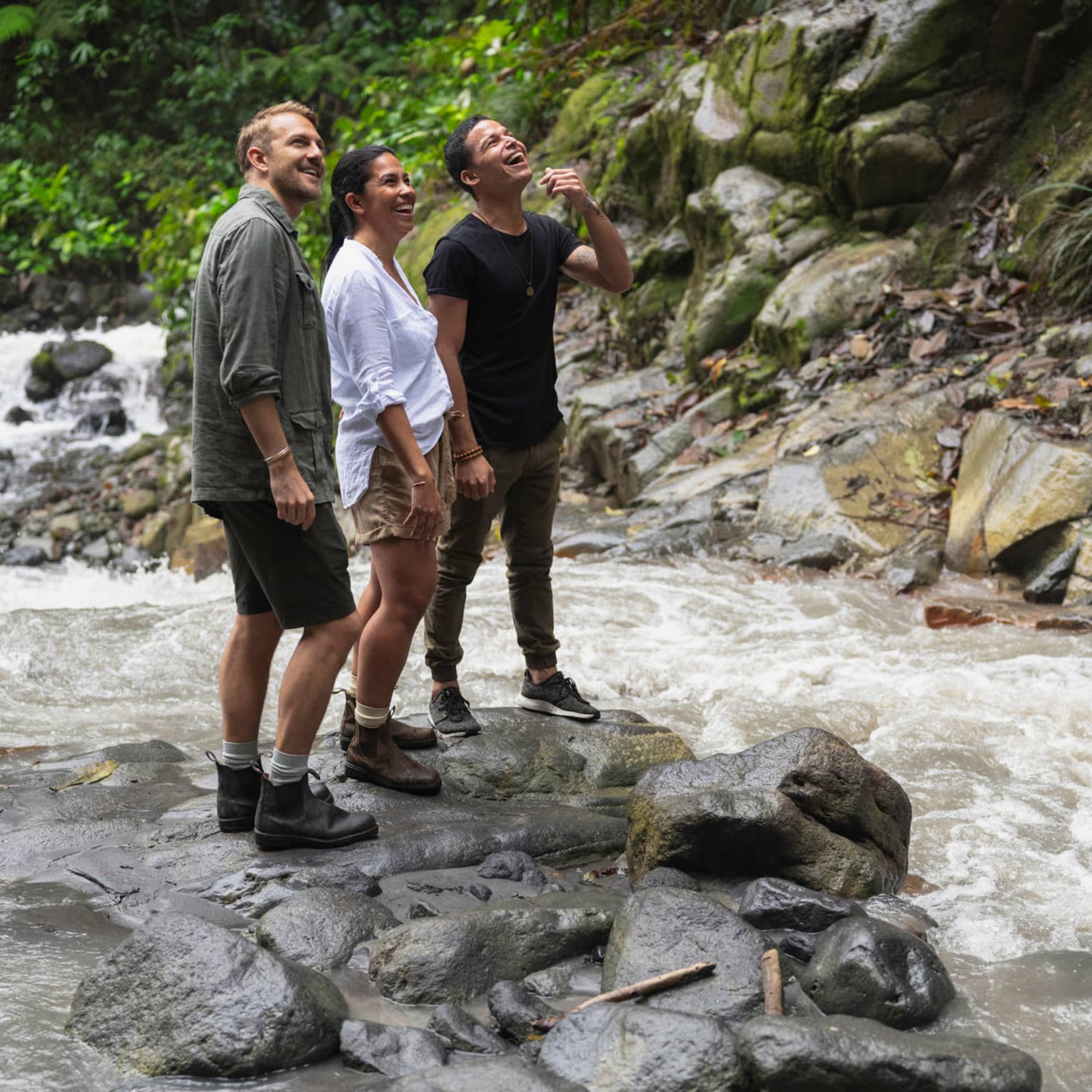 ,Three people stand together on some rocks in the middle of a river as they all look up at the sky