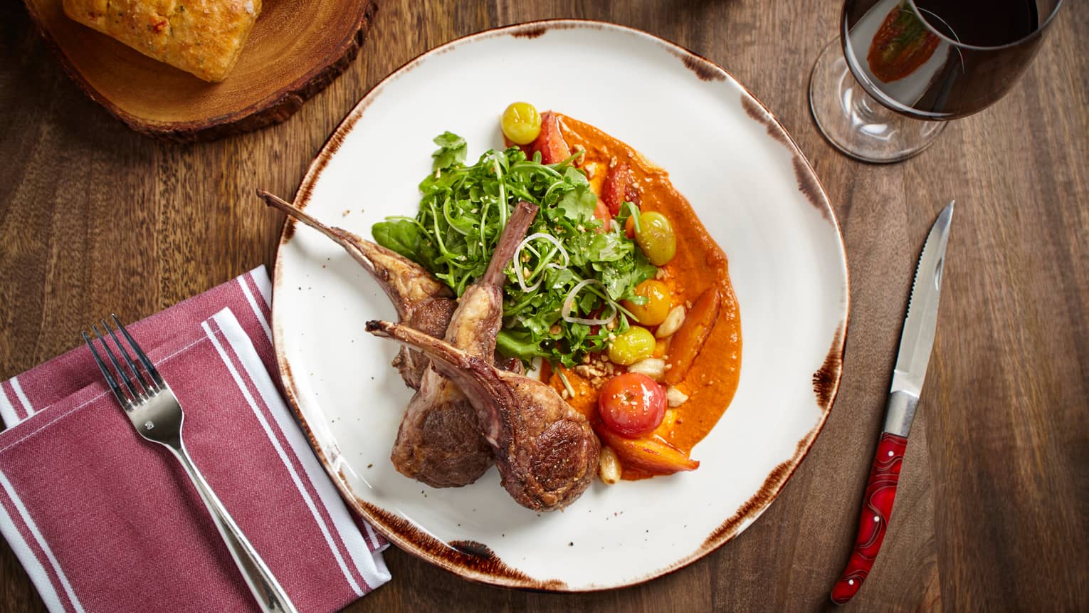 Looking down at white plate with seared lamb chops, greens and roasted vegetables in orange sauce 