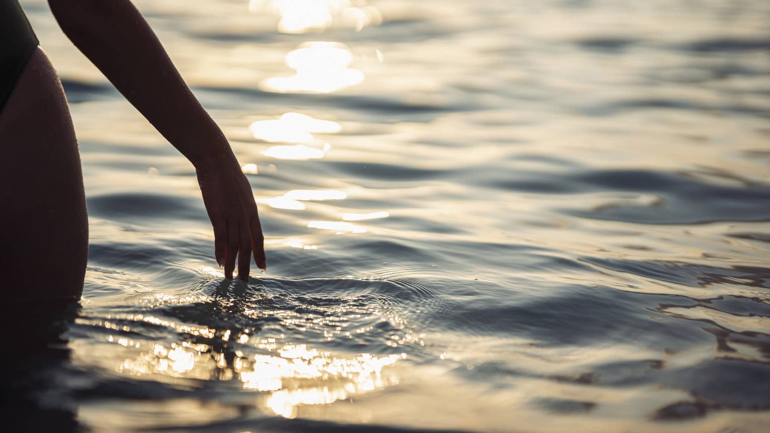 A woman's hand touching ocean water.