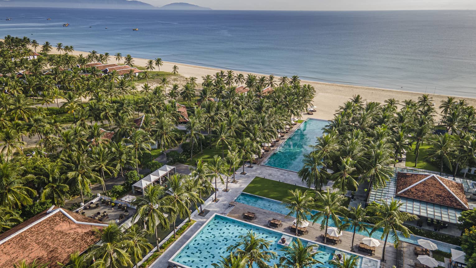 Aerial view of the resort pools with ocean views, palm trees and blue skies