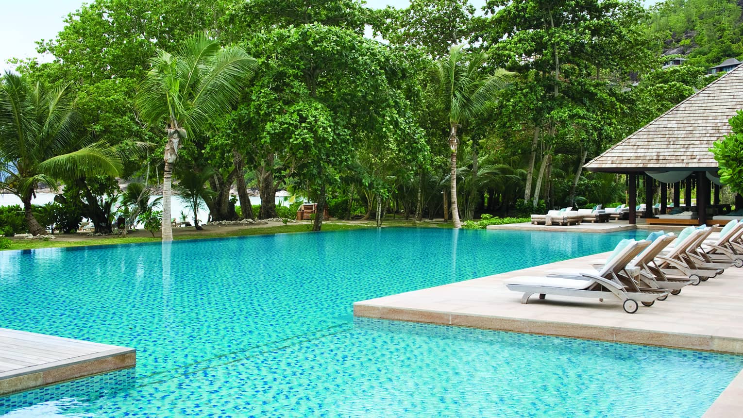 Row of white pool lounge chairs along side of swimming pools, palm trees in background