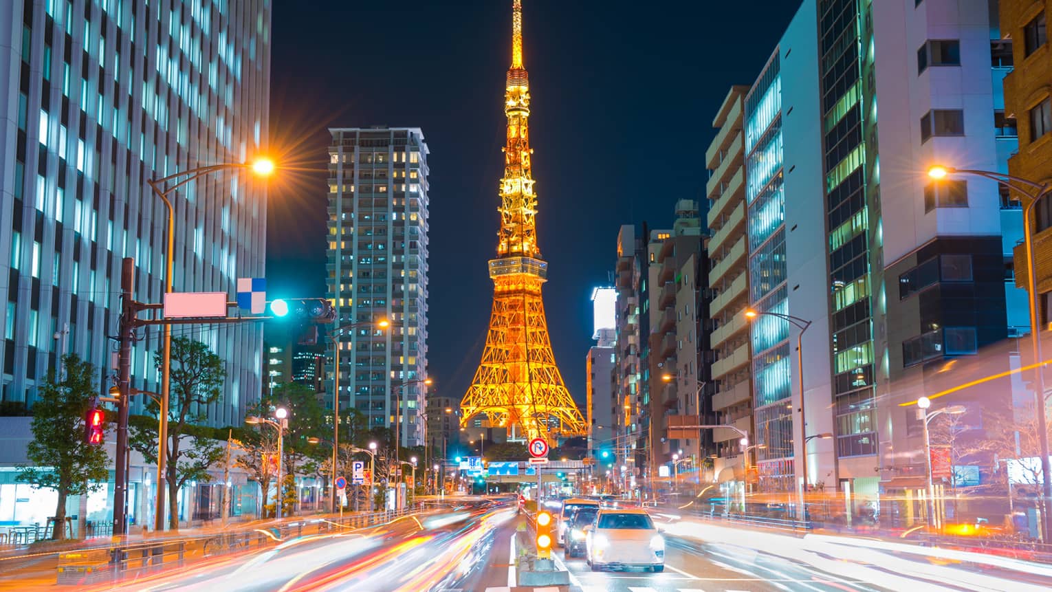 Long view down a brightly-lit street, the Tokyo Tower at the bottom, glowing in orangey hues against an inky-black sky.