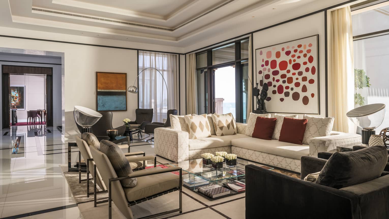 Hotel suite living room with white walls filled with colourful art, a large light-coloured sofa, various arm chairs and a separate seating area