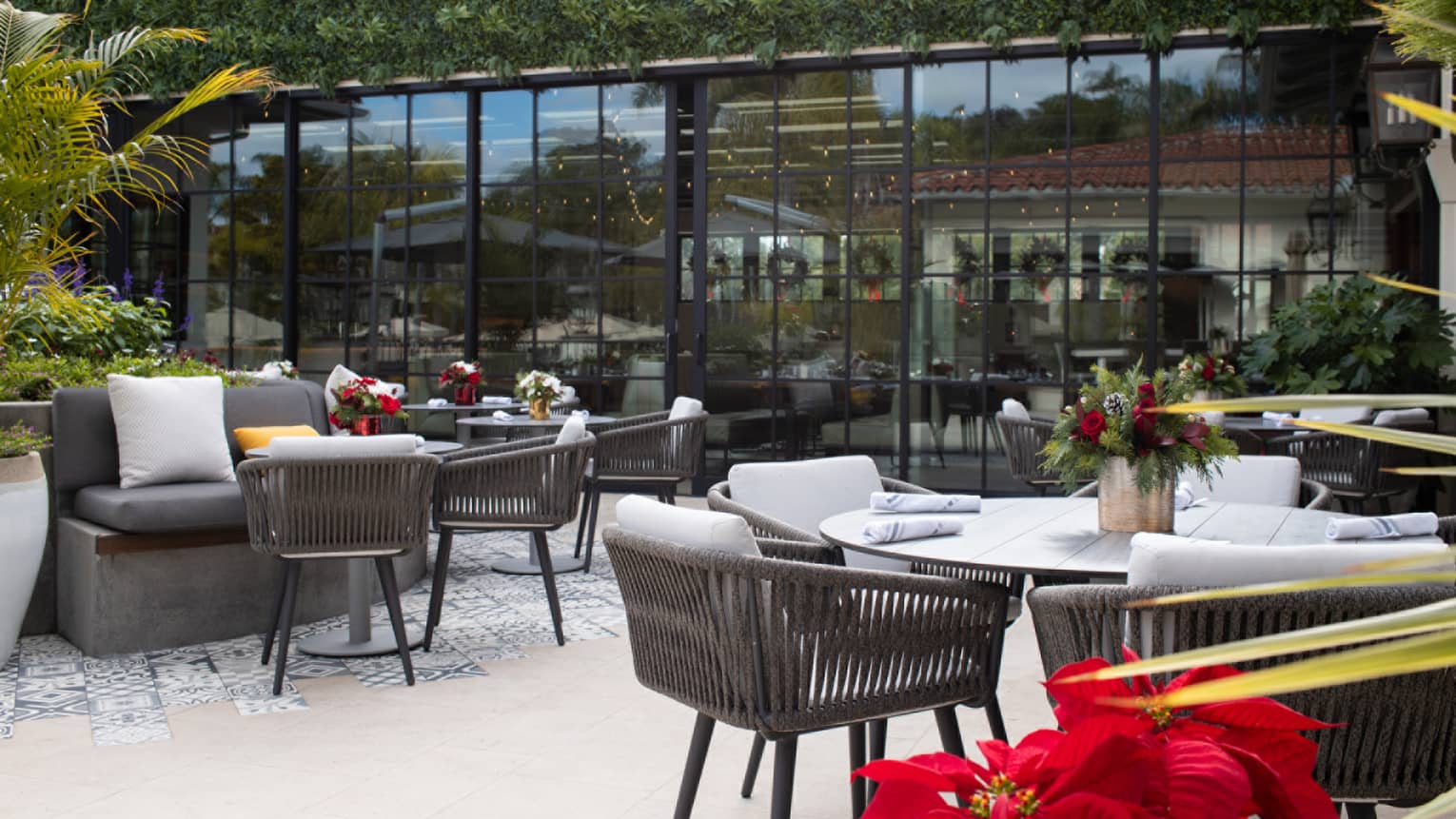 Outdoor patio with gray chairs, greenery and red flowers.