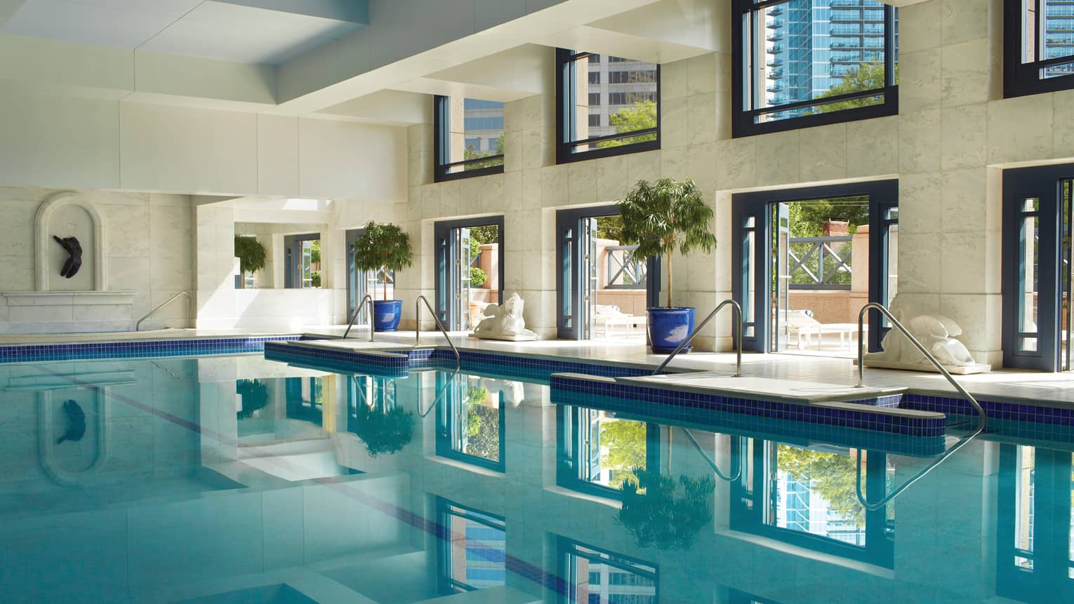 Saltwater lap swimming pool under white marble walls, tall sunny windows