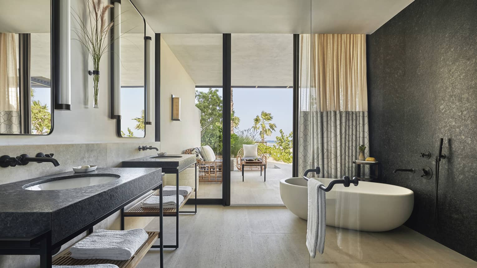 A bathroom with large sliding glass door leading to a sitting area, a bathtub and two sinks.