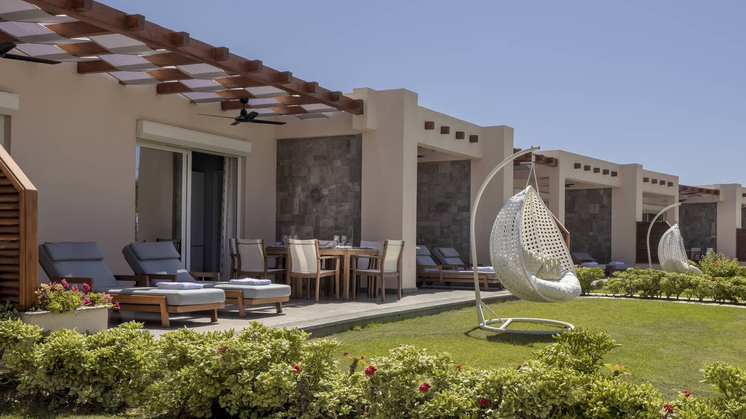 Suite patio and yard with blue lounge chairs and white egg chair, shrubbery