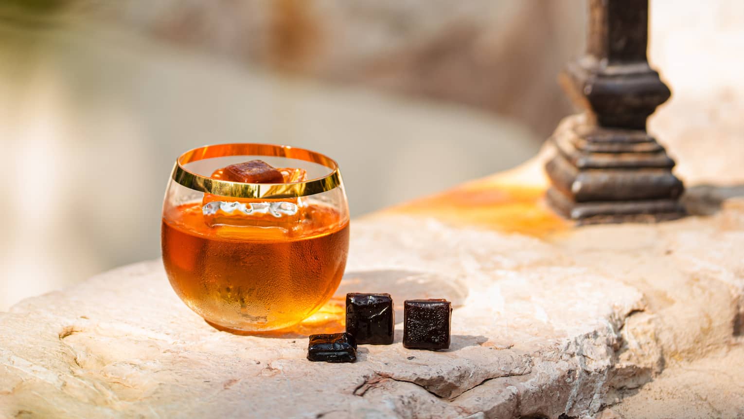 A glass of amber coloured alcohol on a stone wall.