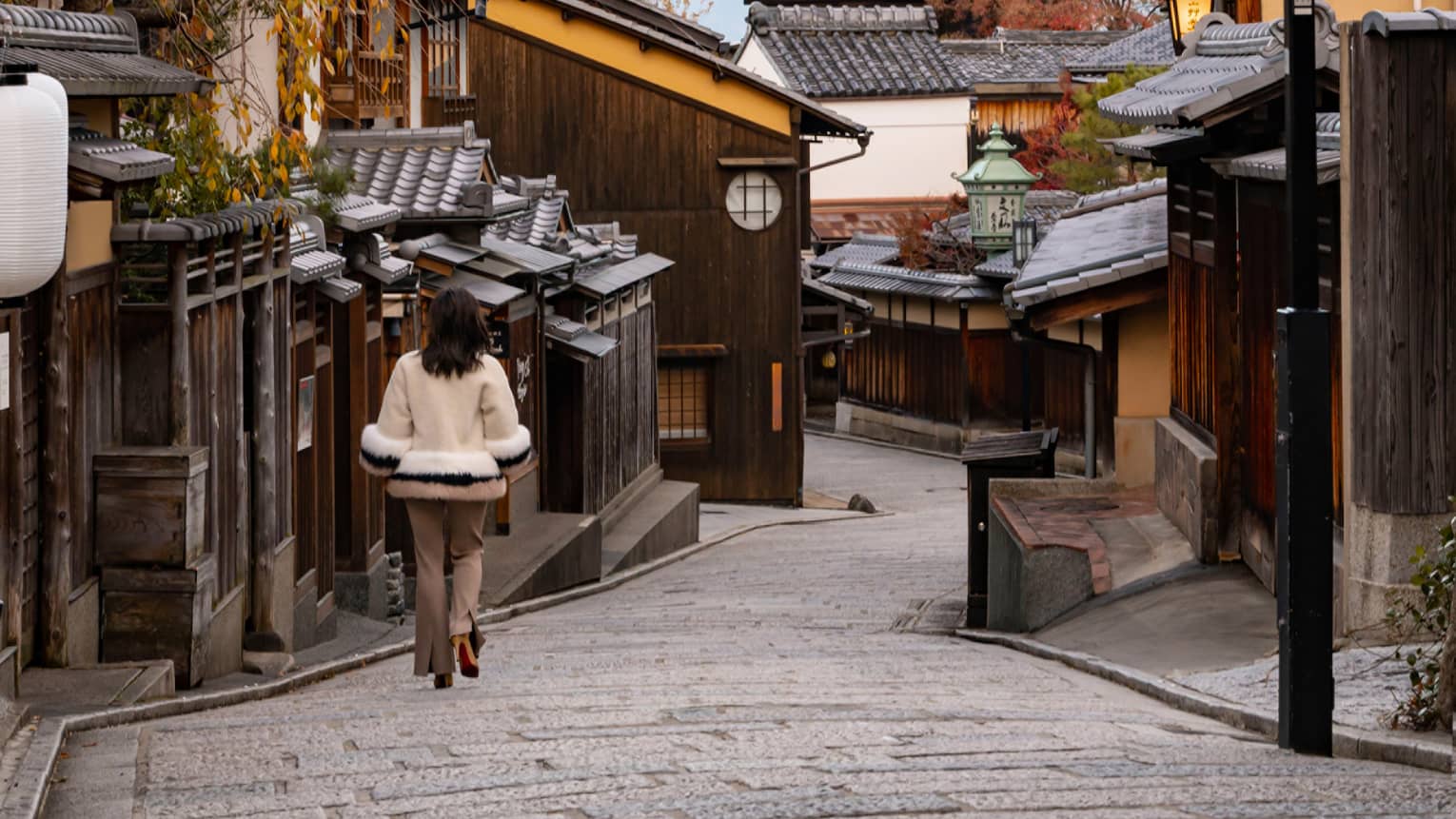 Woman walks down cobblestone street in Kyoto towards Japanese pagoda