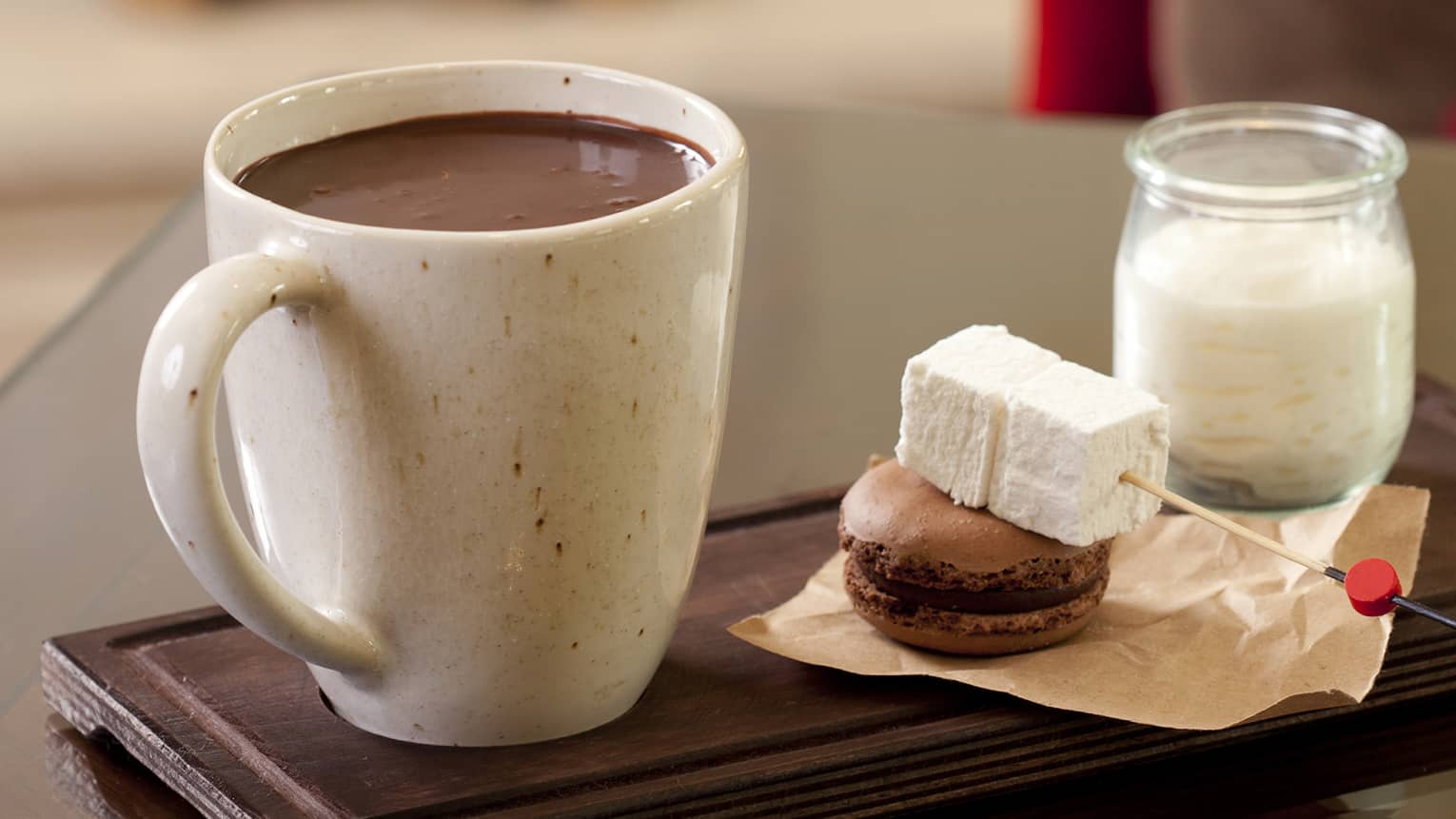 Hot chocolate in large mug beside marshmallow skewer, macaron