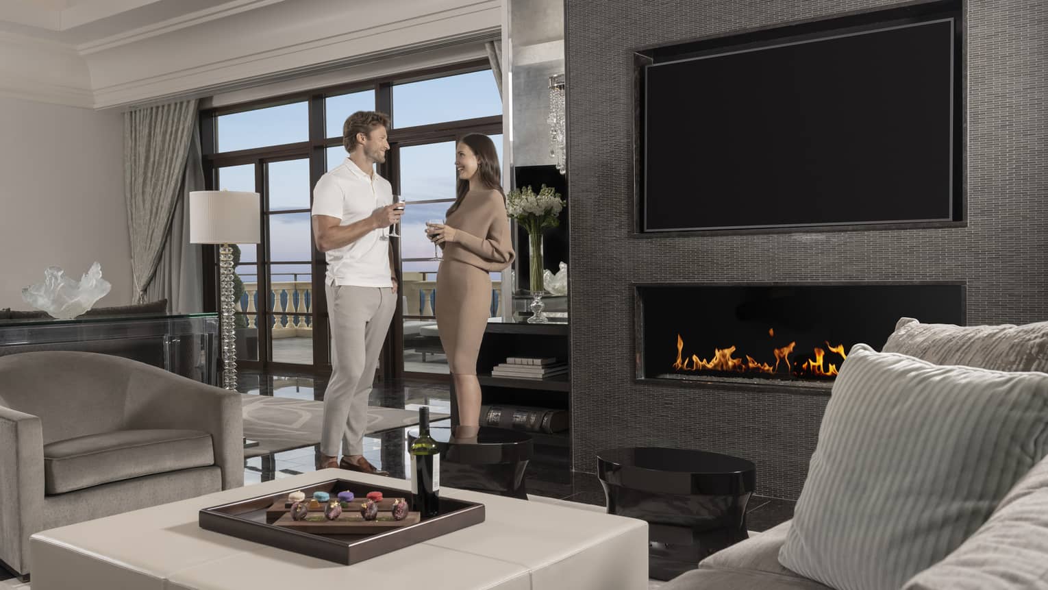 Man and woman stand with drink in hand next to rectangular built-in fireplace