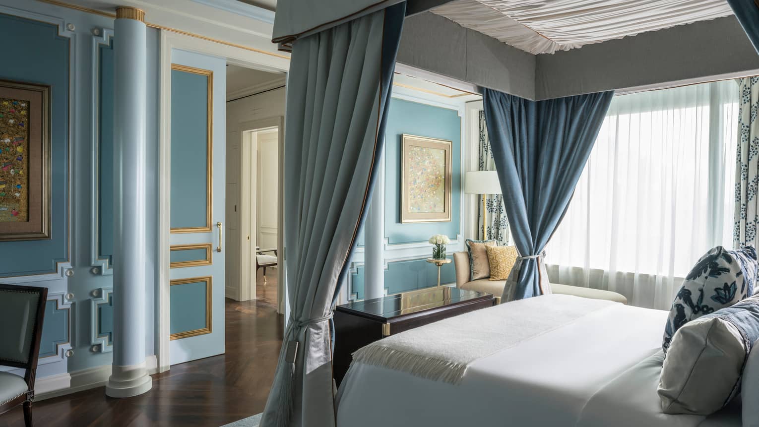 Canopy bed with white linens across from blue wall with pillar