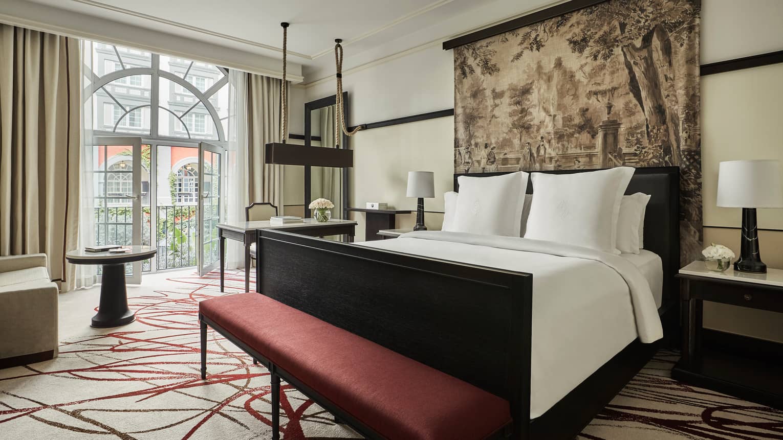Premier Room bed under print headboard, red bench at foot, sunny arched balcony glass doors