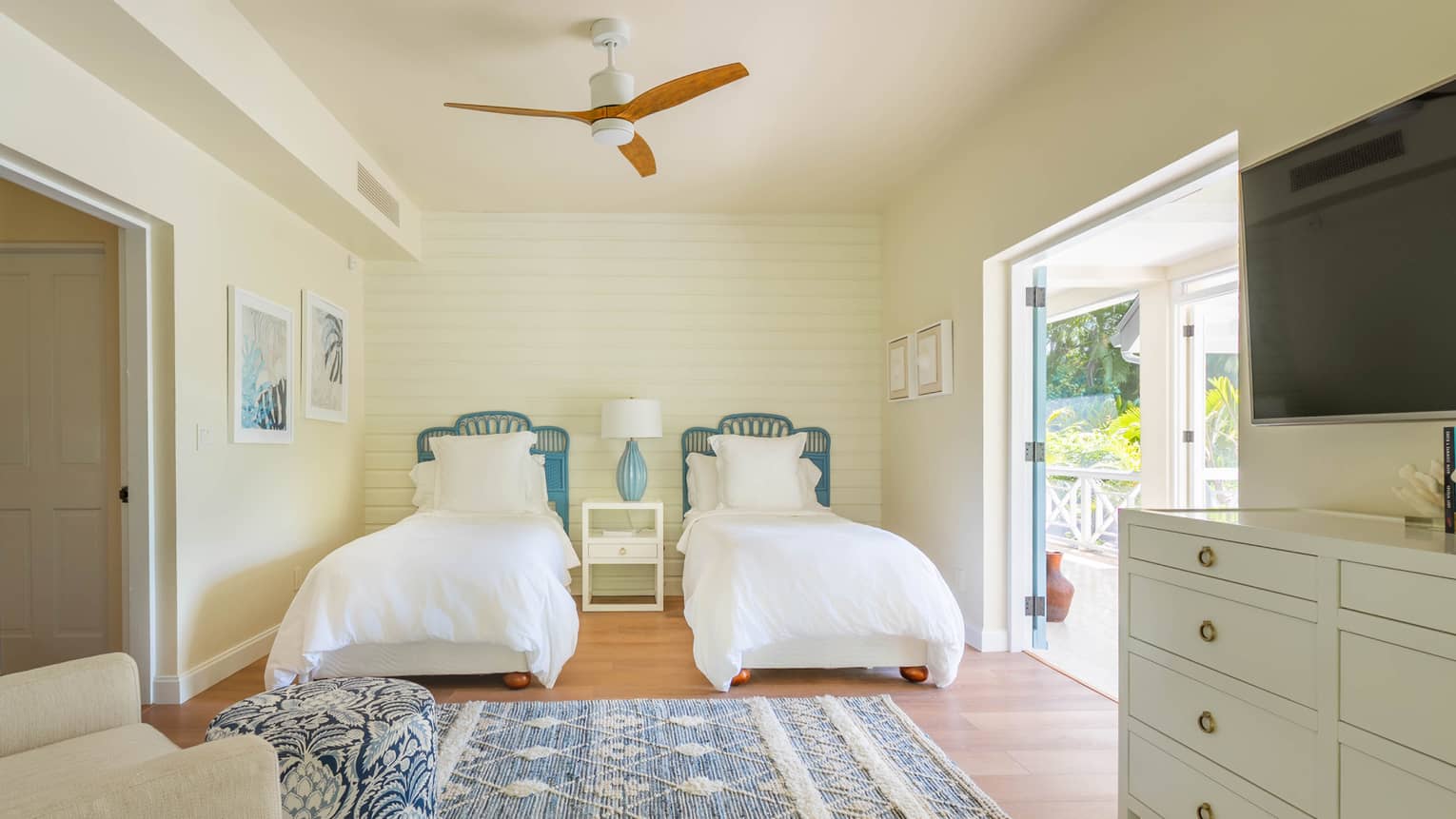 Bedroom with two twin beds, cream-coloured walls, blue and white area rug, dresser, TV and walk-out terrace