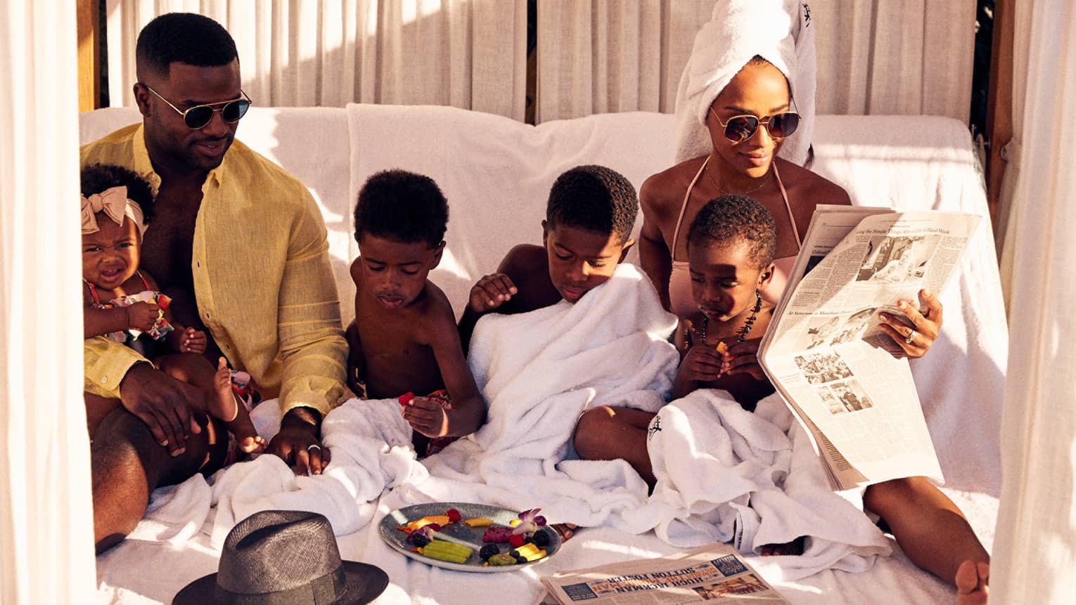 A family of a father, mother and four children lounging on a beach bed outside.