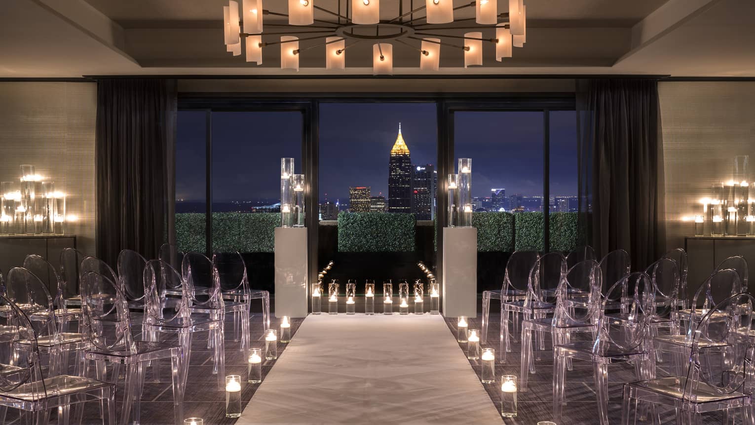 Translucent chairs are arranged in rows and candles line a pathway to the front of the ballroom