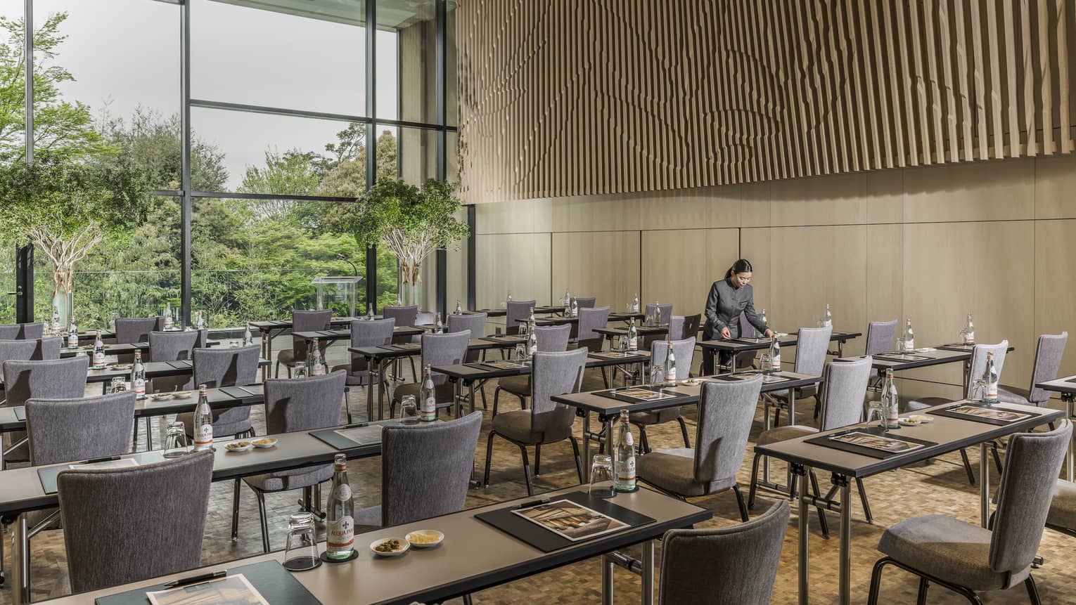 Rows of meeting tables and chairs facing window, hotel staff places agenda on table