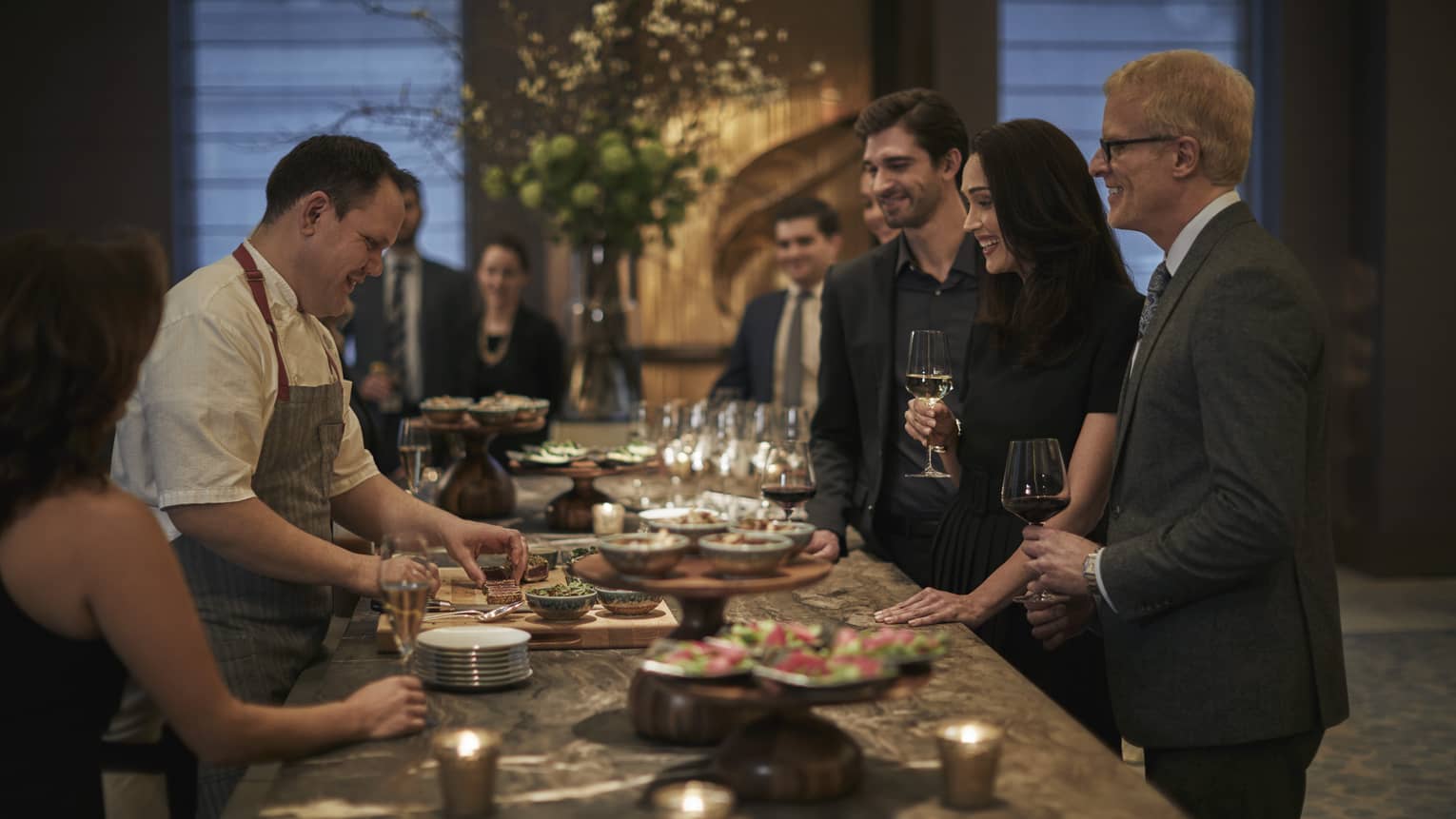 Culinary team and group examine, taste menu and wine at long buffet table