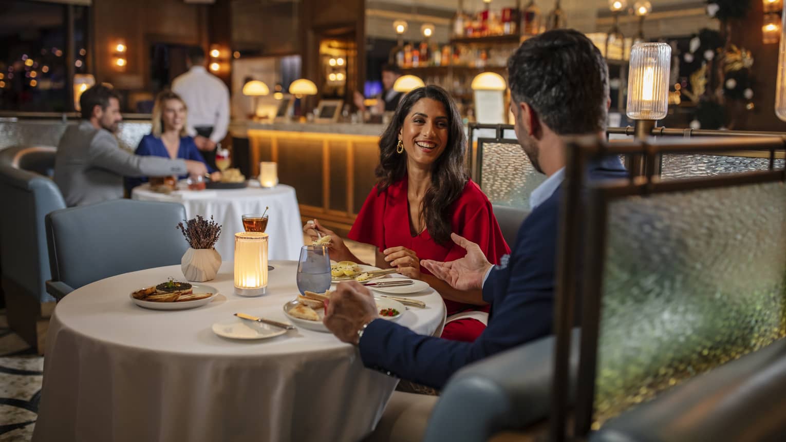 Woman in red dress, smiling at man, seated at round dining table in bar lounge