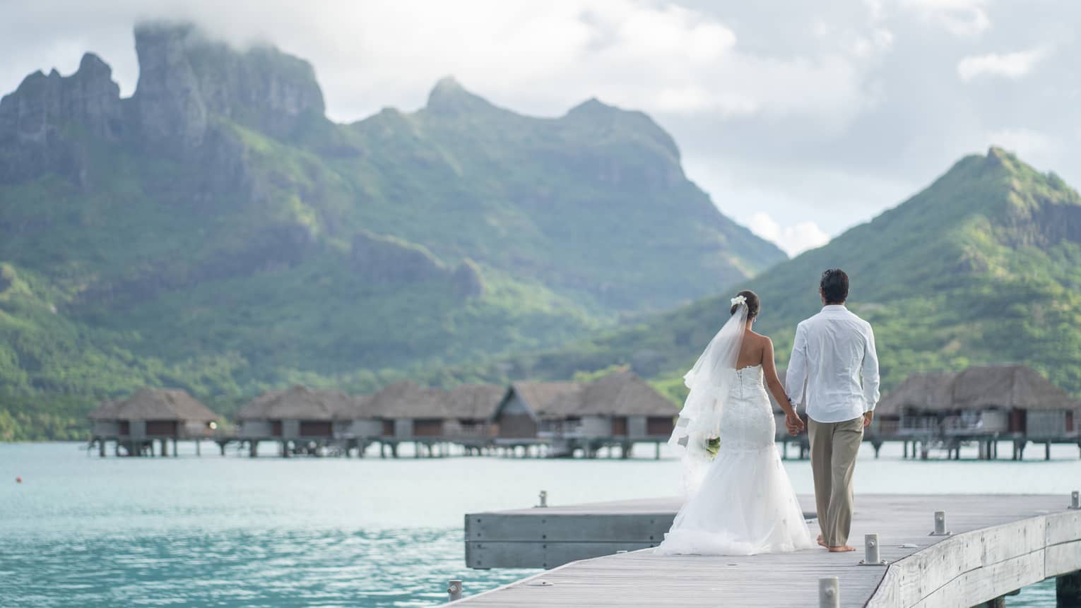 Bride and groom on overwater bungalow walkway, Bora Bora mountains in background