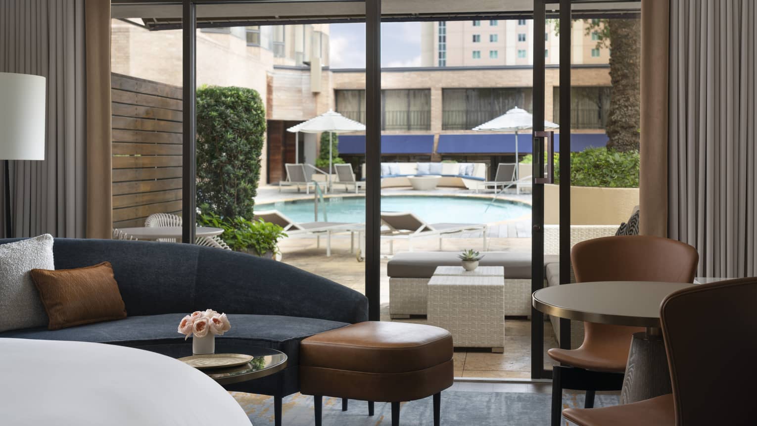 Hotel room with chaise lounge and two chairs, opening to private patio with pool view