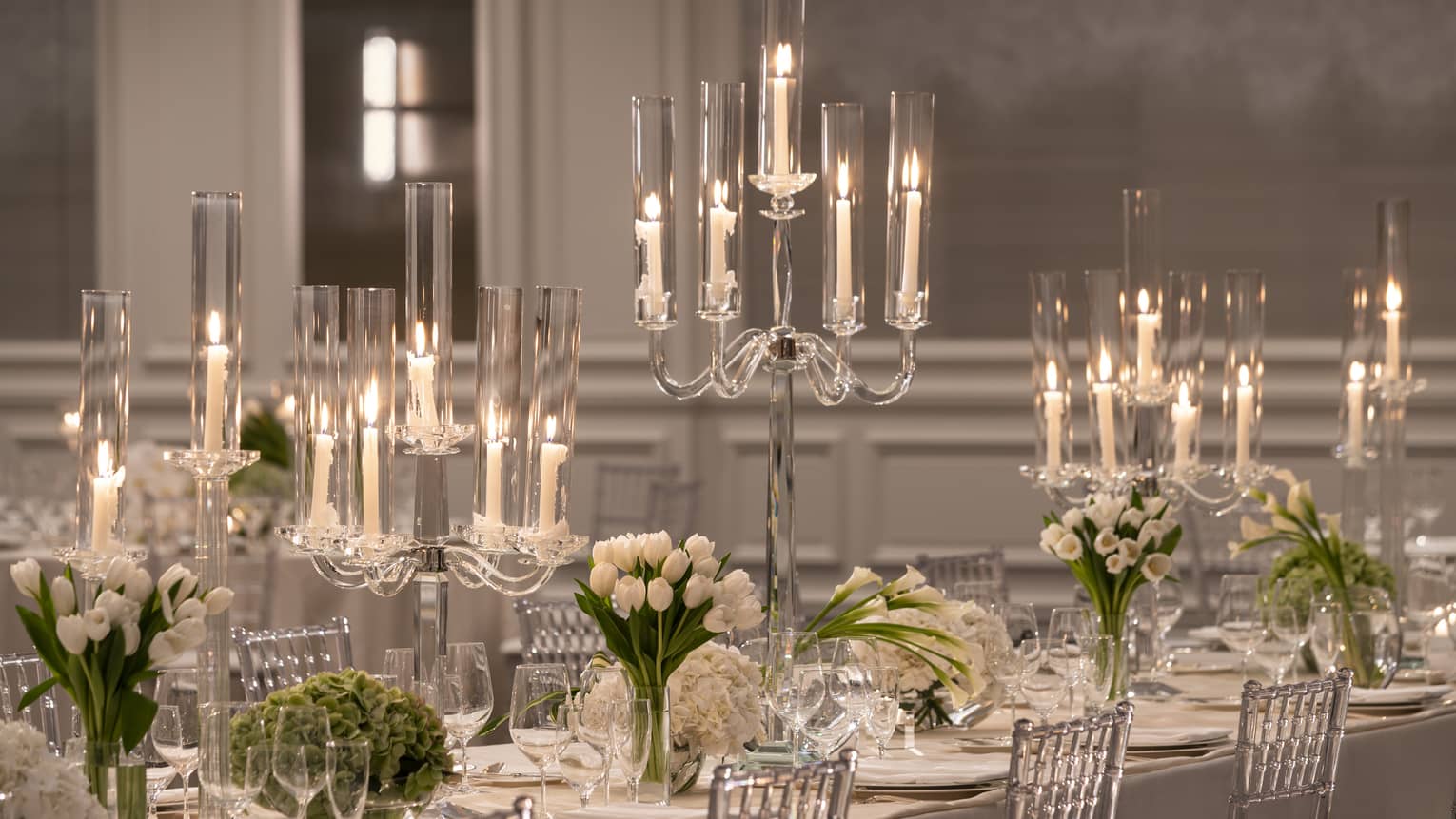 Formally set white dining table with candelabras and white flowers flanked by silver chairs