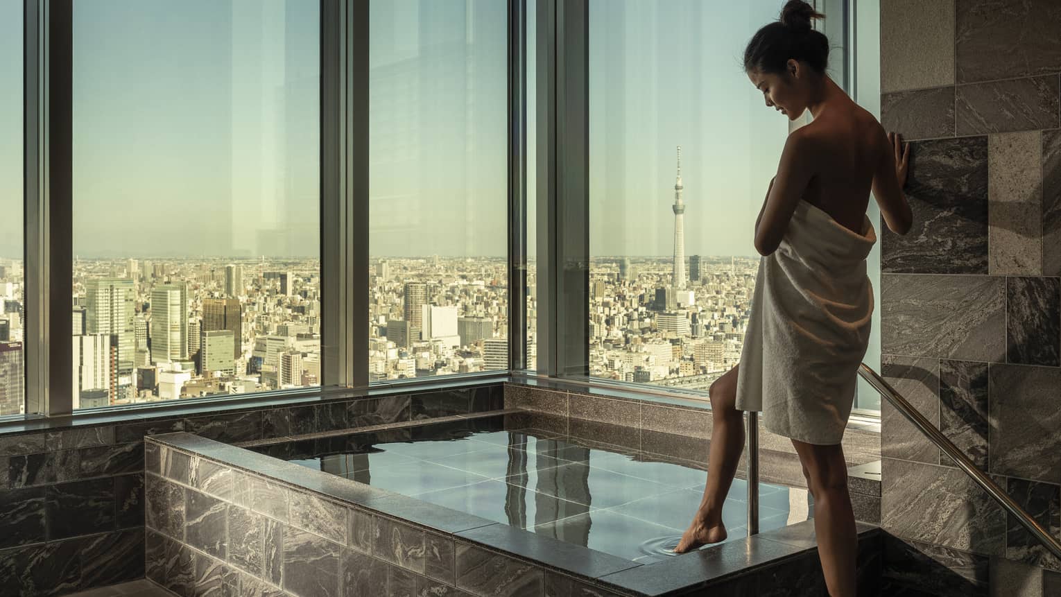 Woman wrapped in white towel dips her toe into the ofuro bath