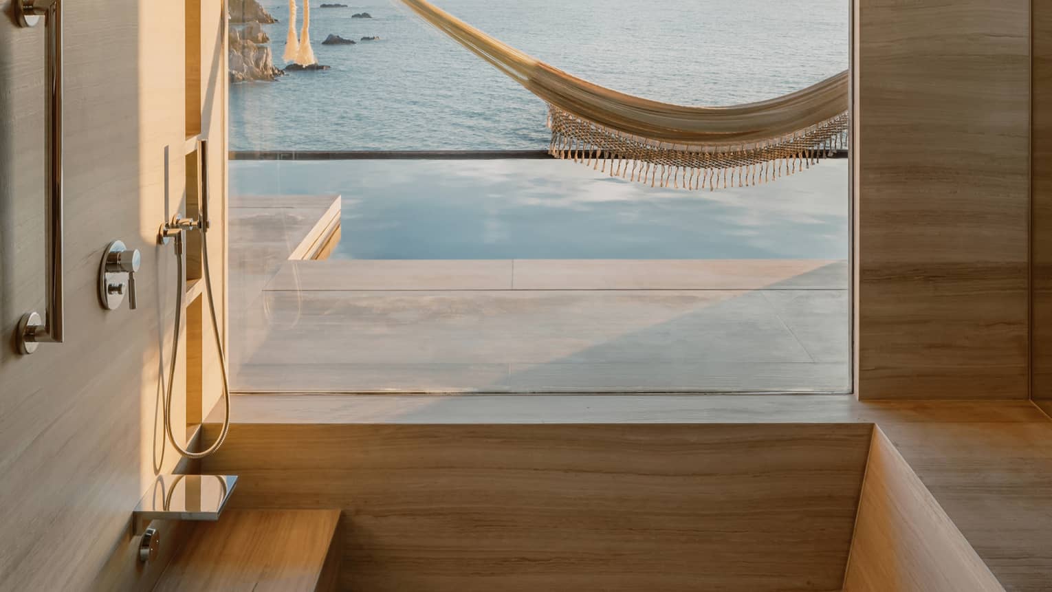 Minimalist bathroom with a deep tub and a large window offering a breathtaking view of an infinity pool, a hammock and the ocean stretching towards the horizon