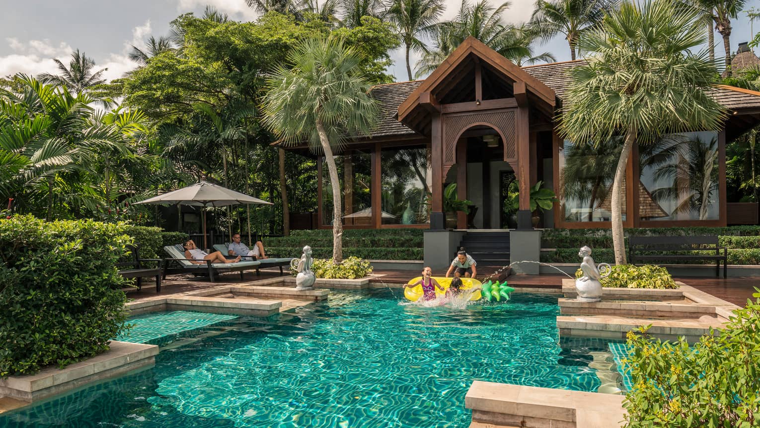 Family swims under monkey fountains in private residence outdoor swimming pool