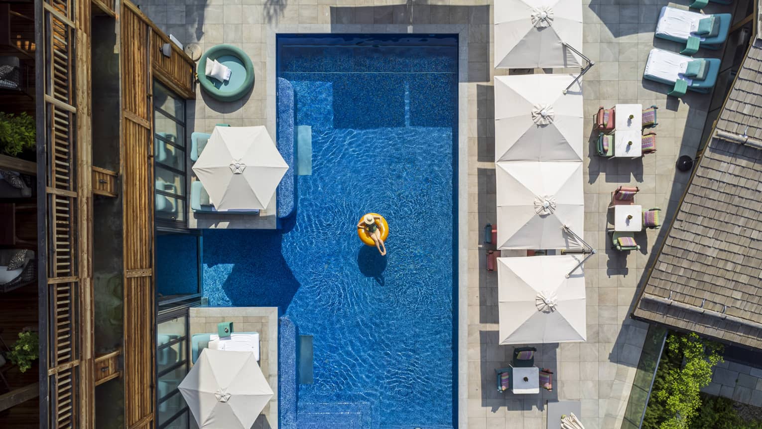 A person in a tube in an outdoor pool surrounded by umbrellas and chairs.