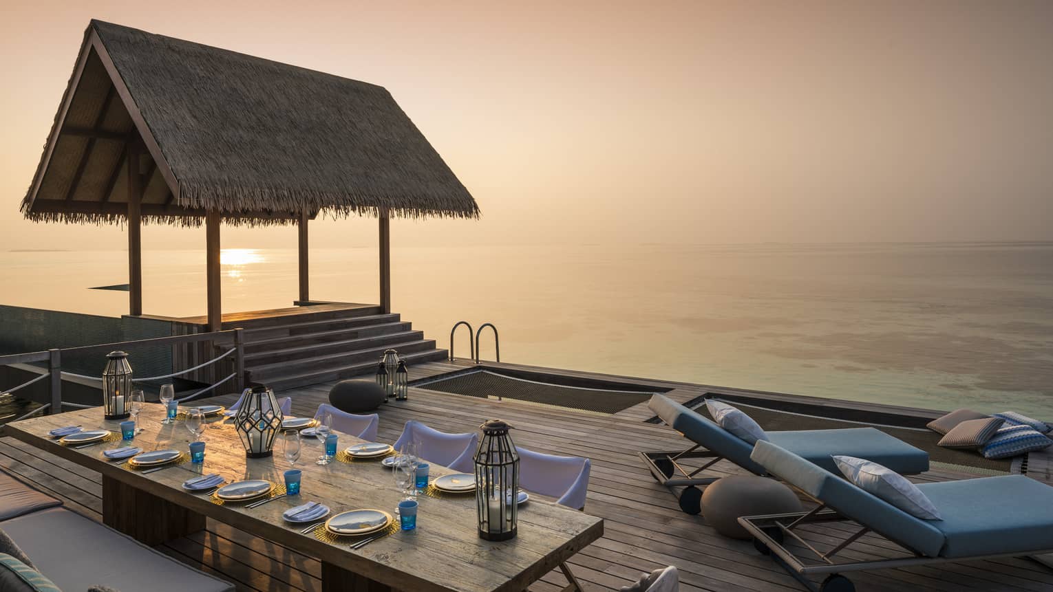 Two-Bedroom Water Villa thatched roof pavilion over long private dining table on deck at sunset