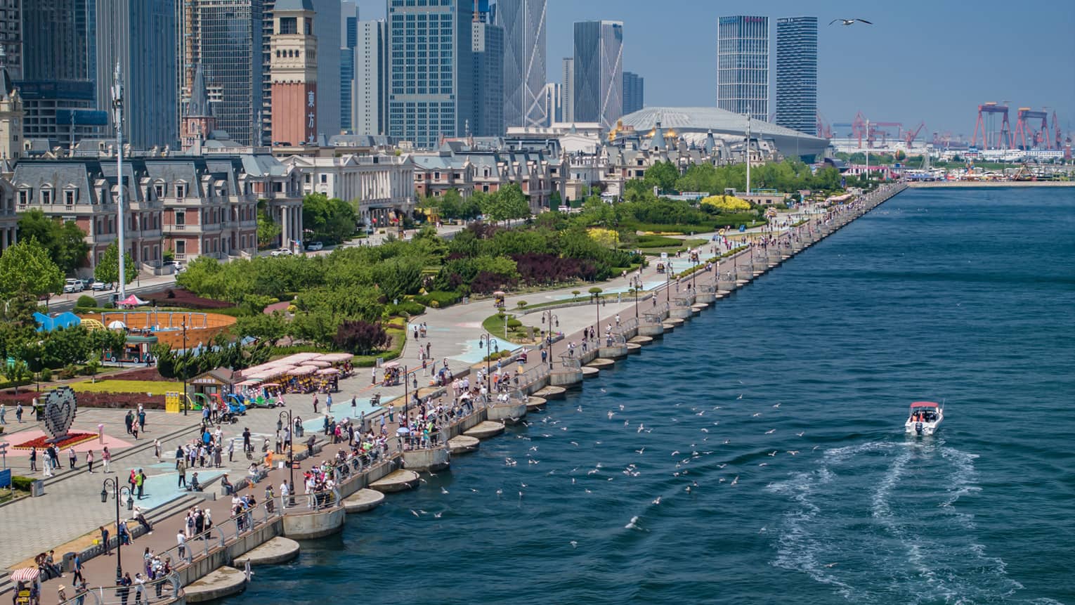 Aerial view of water along the pier of a bustling boulevard bordered by lush parkland, old buildings and modern high-rises.