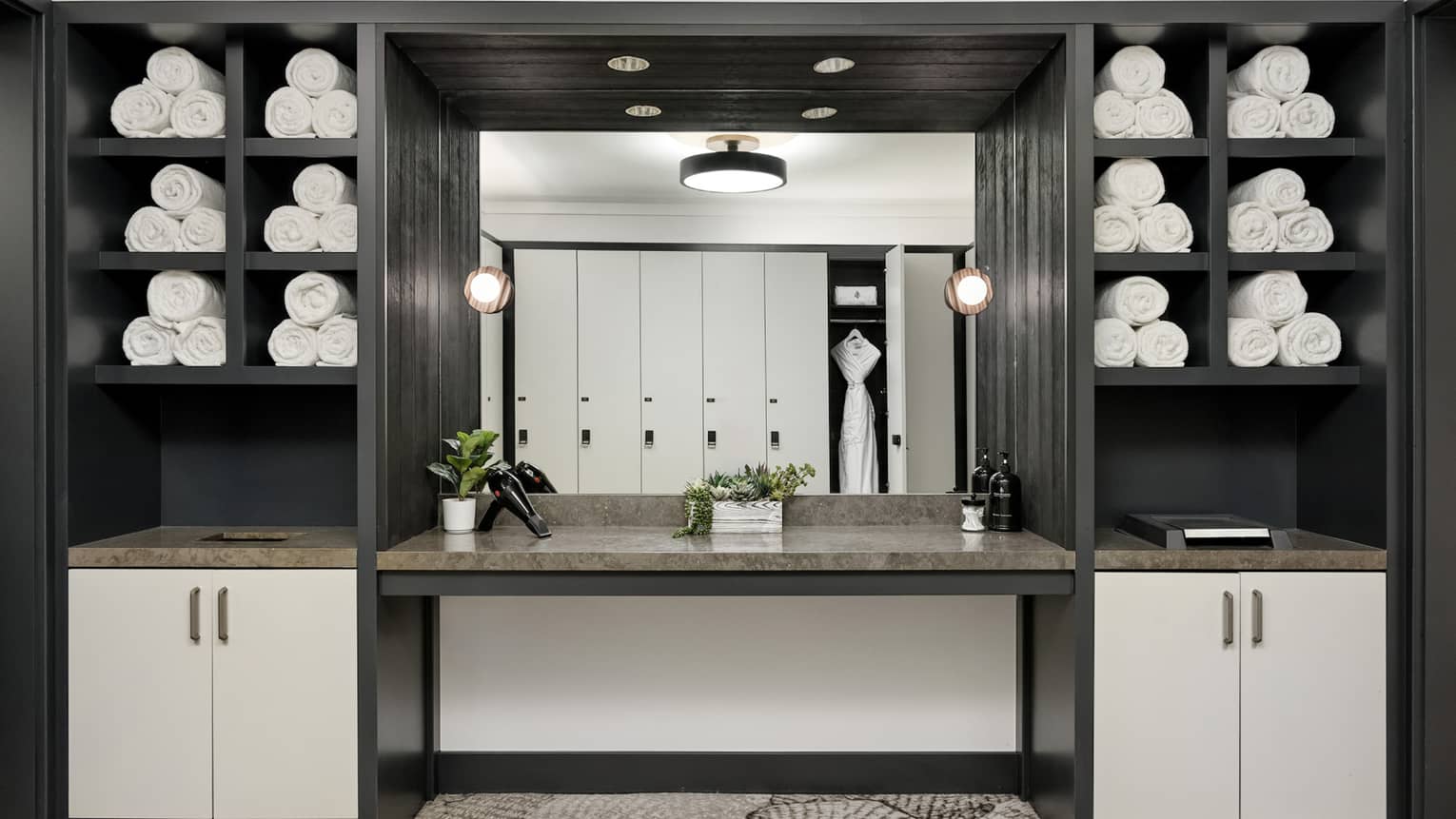 Built-in dark wood shelves with rolled towels in cubbies, mirror showing lockers on opposite wall