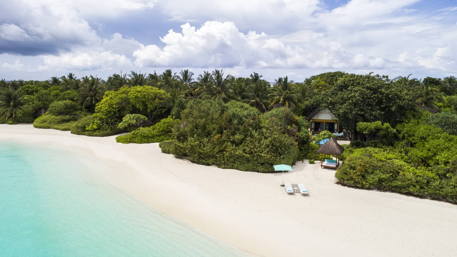 Quiet white-sand beach in the Maldives with turquoise water and lush green trees inland