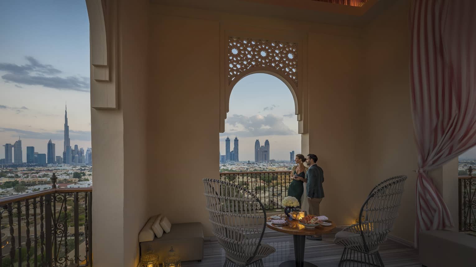 A man and woman lean against a wall of an outdoor terrace an peer through an opening, over the city in Dubai at Jumeirah Beach