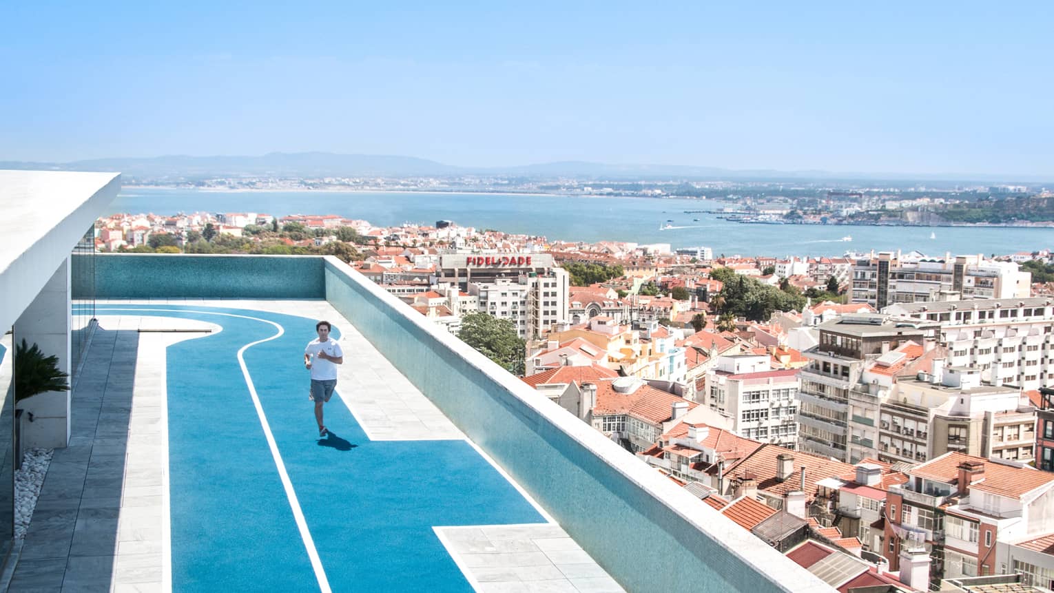 Man in shorts and T-shirt jogs on rooftop running track on sunny day overlooking Lisbon rooftops