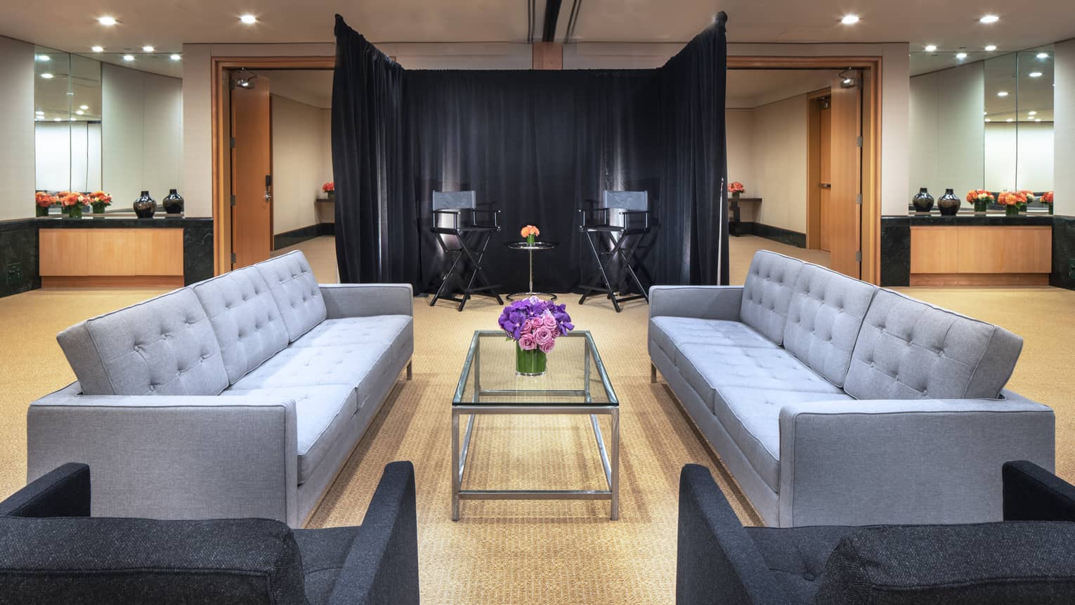Two modern, gray rectangular couches face one another with a purple floral arrangement on top of a glass table in between them