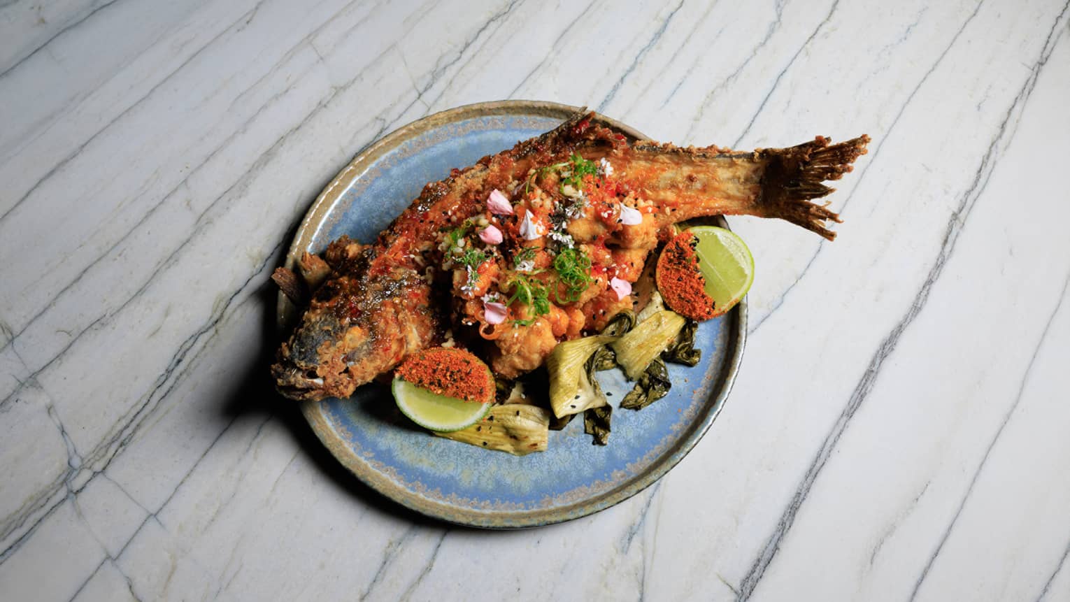 Branzino Chicharr�n with hot sweet chili sauce, roasted pak choi and sesame seeds served on a blue stoneware plate