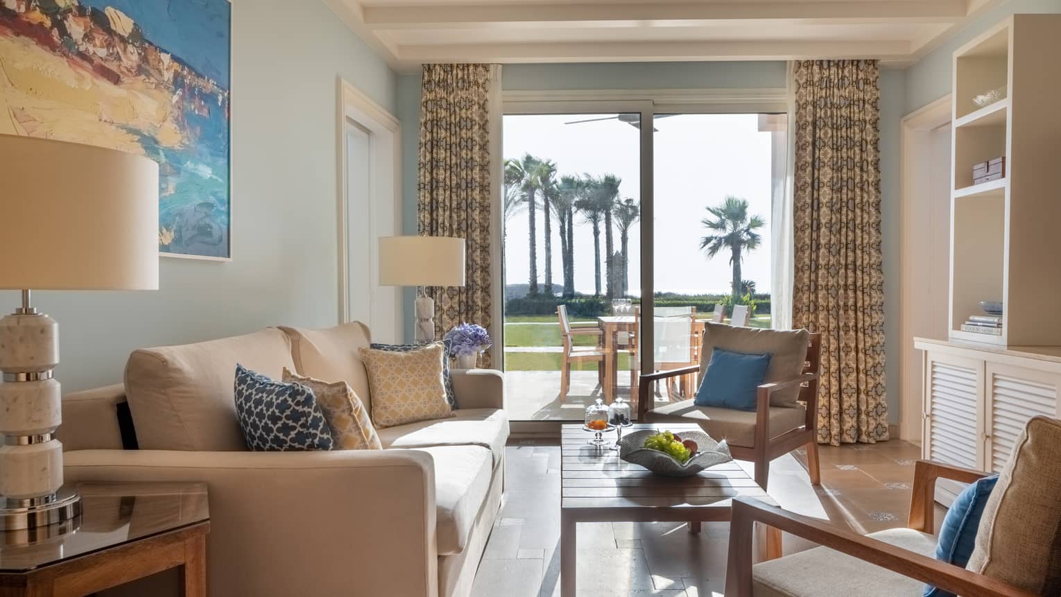 Guest room living area with tan sofa and armchairs, coffee table, sliding glass door to patio
