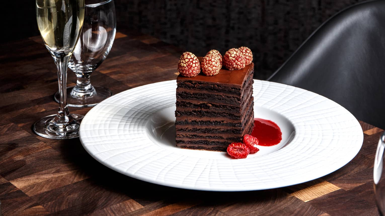 Layered chocolate desert on a white plate next to a flute of champagne and glass of water