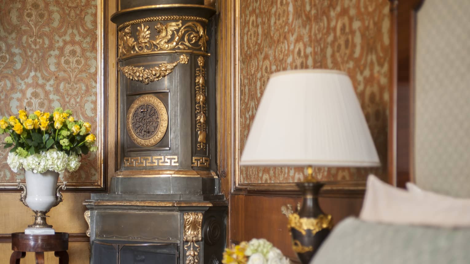 Detailing in a Gallery Suite bedroom, with an ornate hearth, copper-coloured floral wallpaper, lamp and floral arrangement, at Four Seasons Hotel Florence
