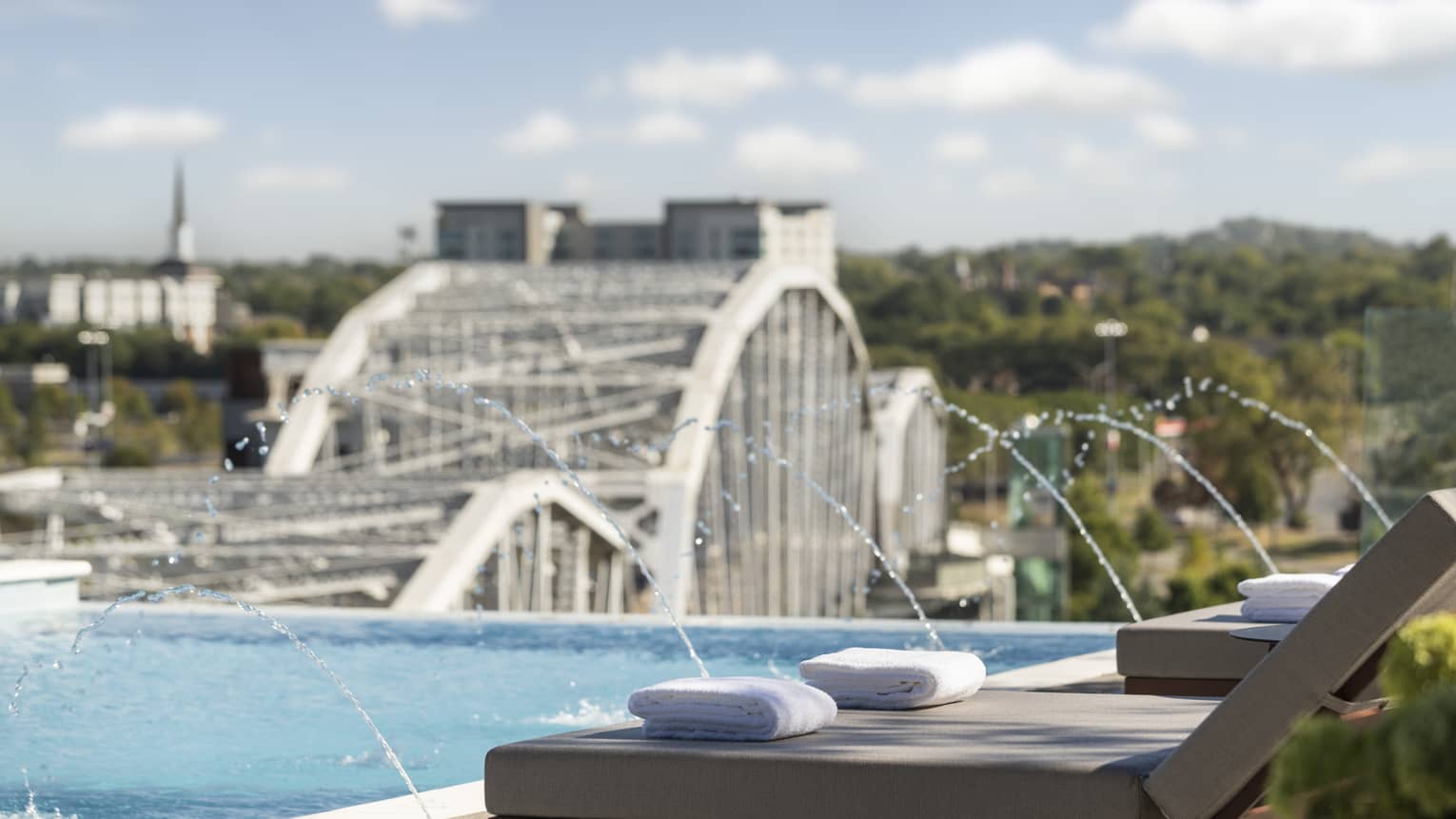 Outdoor pool with water feature, and a city bridge over the river in the background