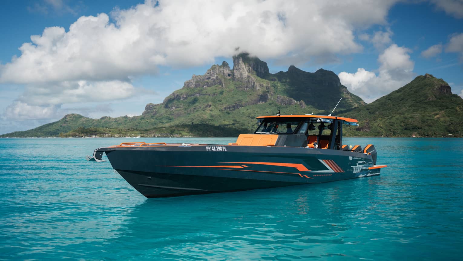 An orange and black yacht charter boar sails in front of a mountain landscape